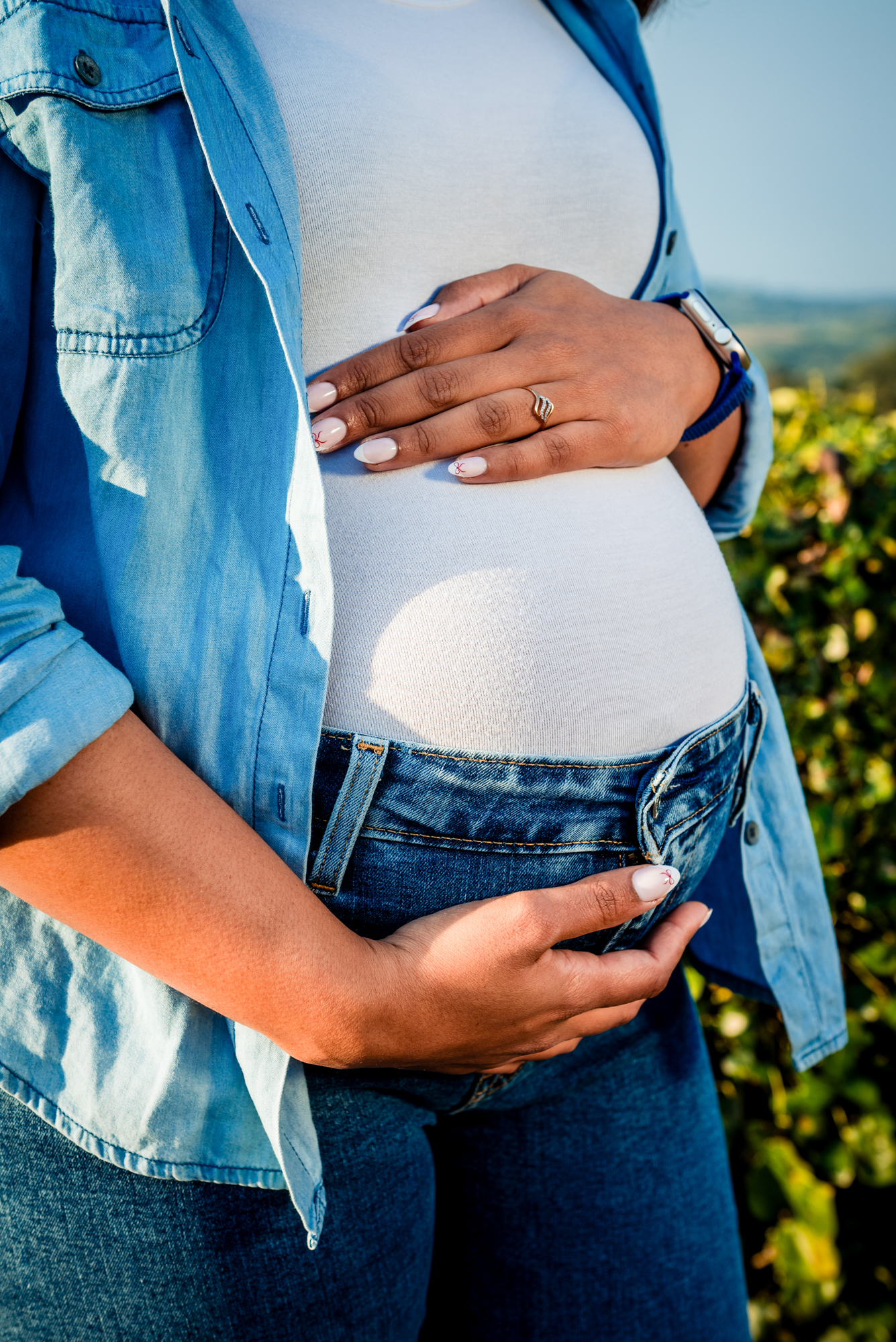 Close-up of pregnant belly in casual outfit with denim shirt and soft natural light.