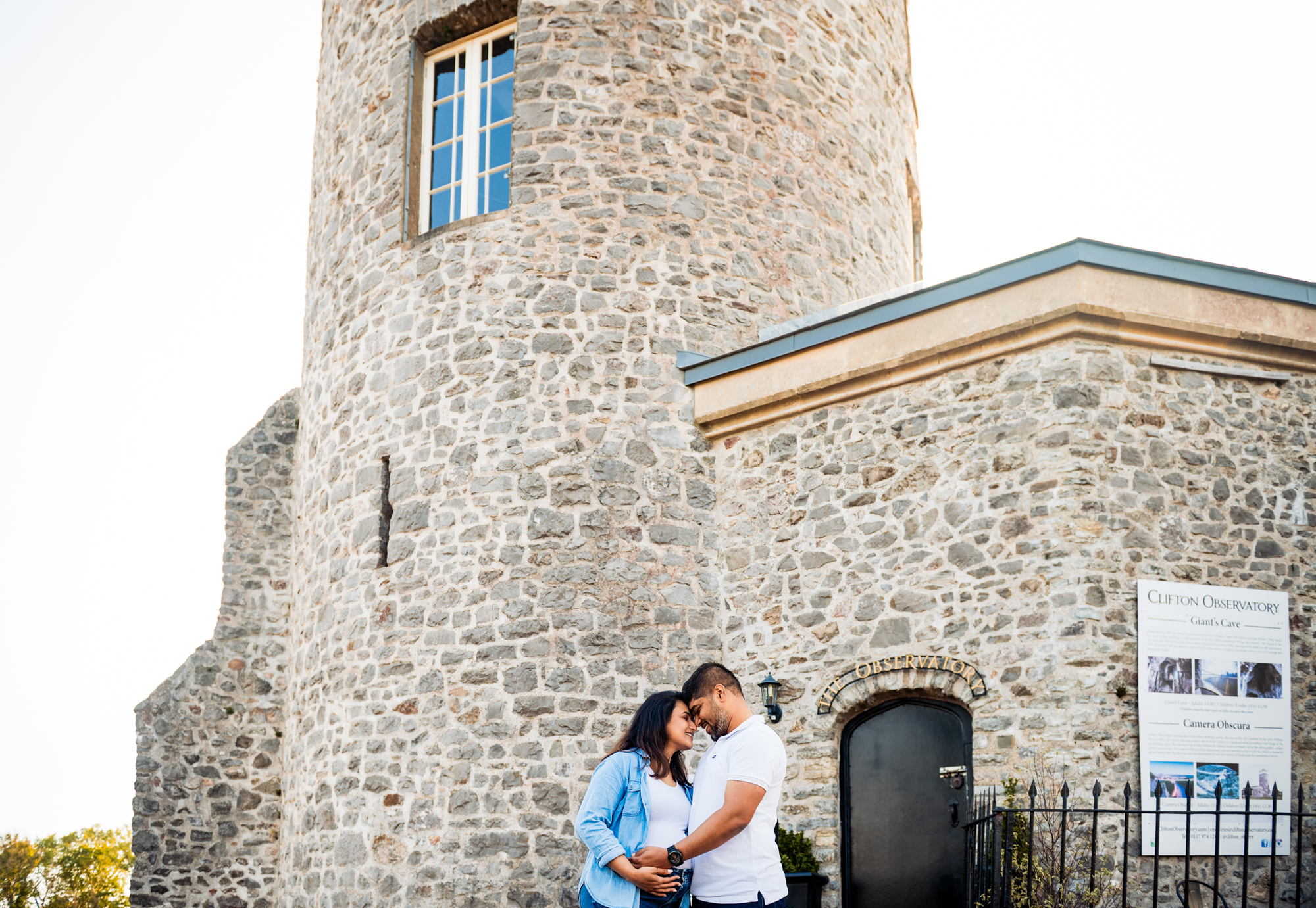 Expectant couple embracing outside Clifton Observatory stone building during maternity photoshoot in Bristol.