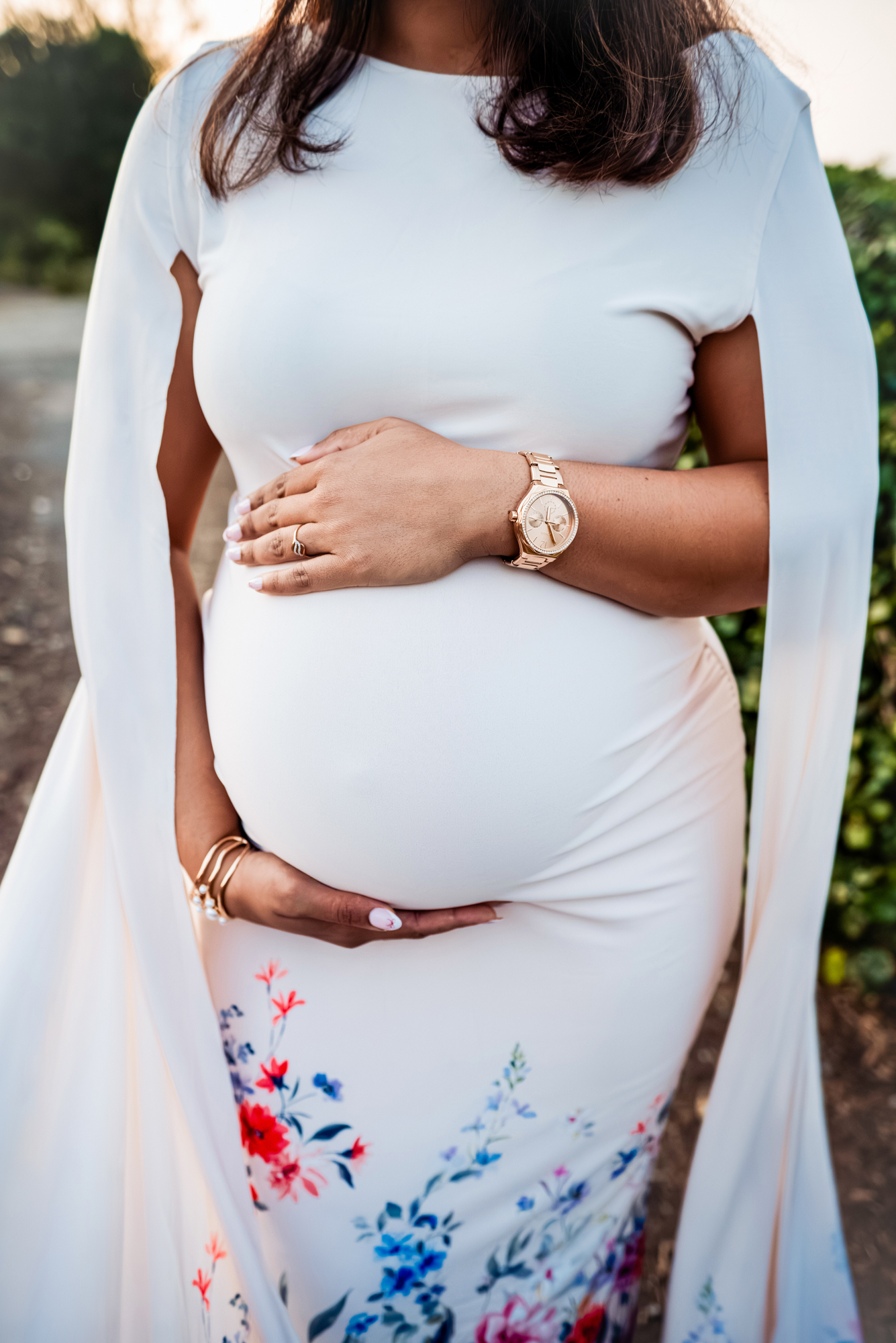Close-up of hands gently holding baby bump in white maternity dress during golden hour in Bristol.