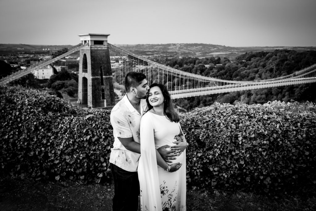 Black and white portrait of couple embracing during maternity photoshoot overlooking Bristol bridge.