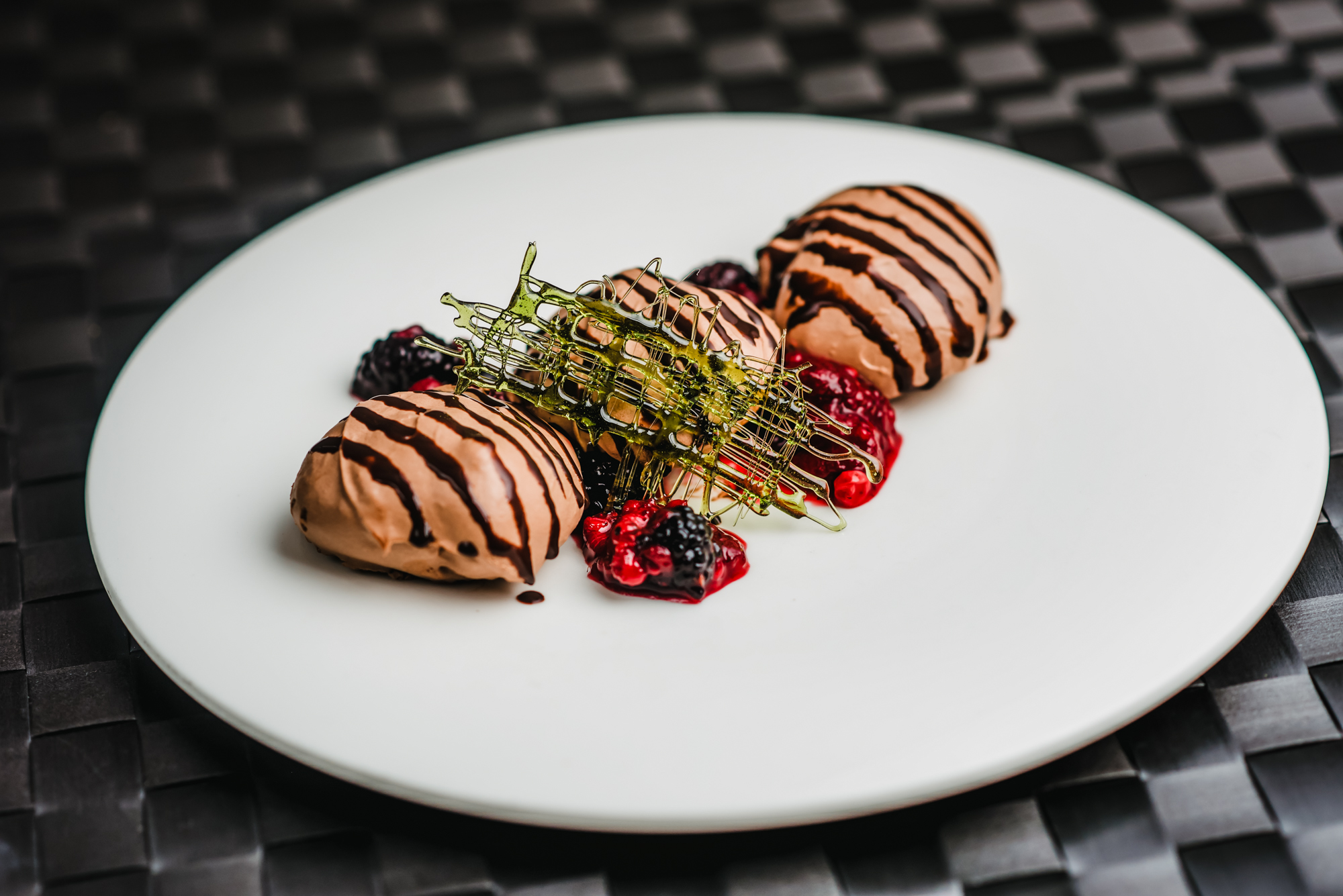 Chocolate mousse quenelles with berry compote and caramel decoration plated for fine dining dessert service.
