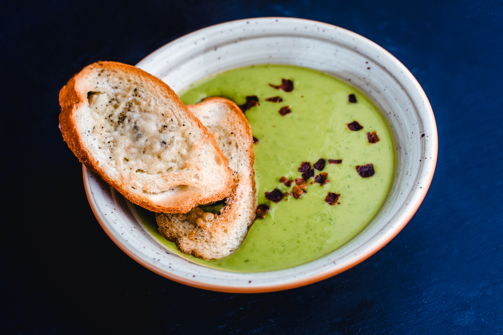 Creamy green vegetable soup topped with crispy bacon and garlic bread slices at Rubin Hotel Budapest Autumn Menu.