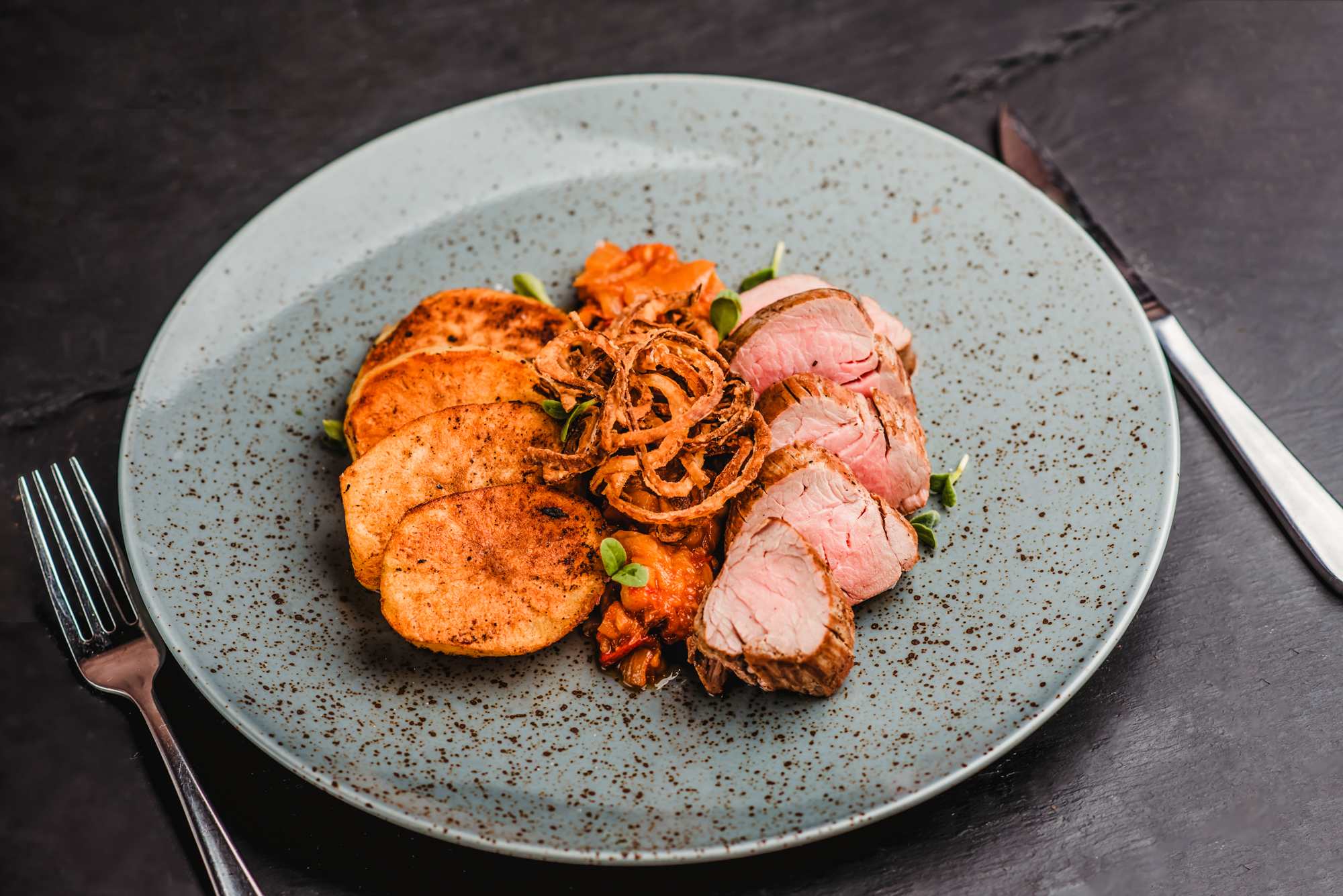 Sliced pork tenderloin with roasted potatoes, crispy onions, and vegetables plated for restaurant dining.