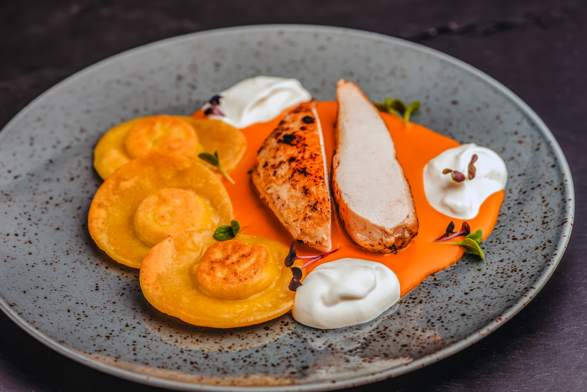 Grilled chicken breast with creamy orange sauce and ravioli plated for modern restaurant dining.