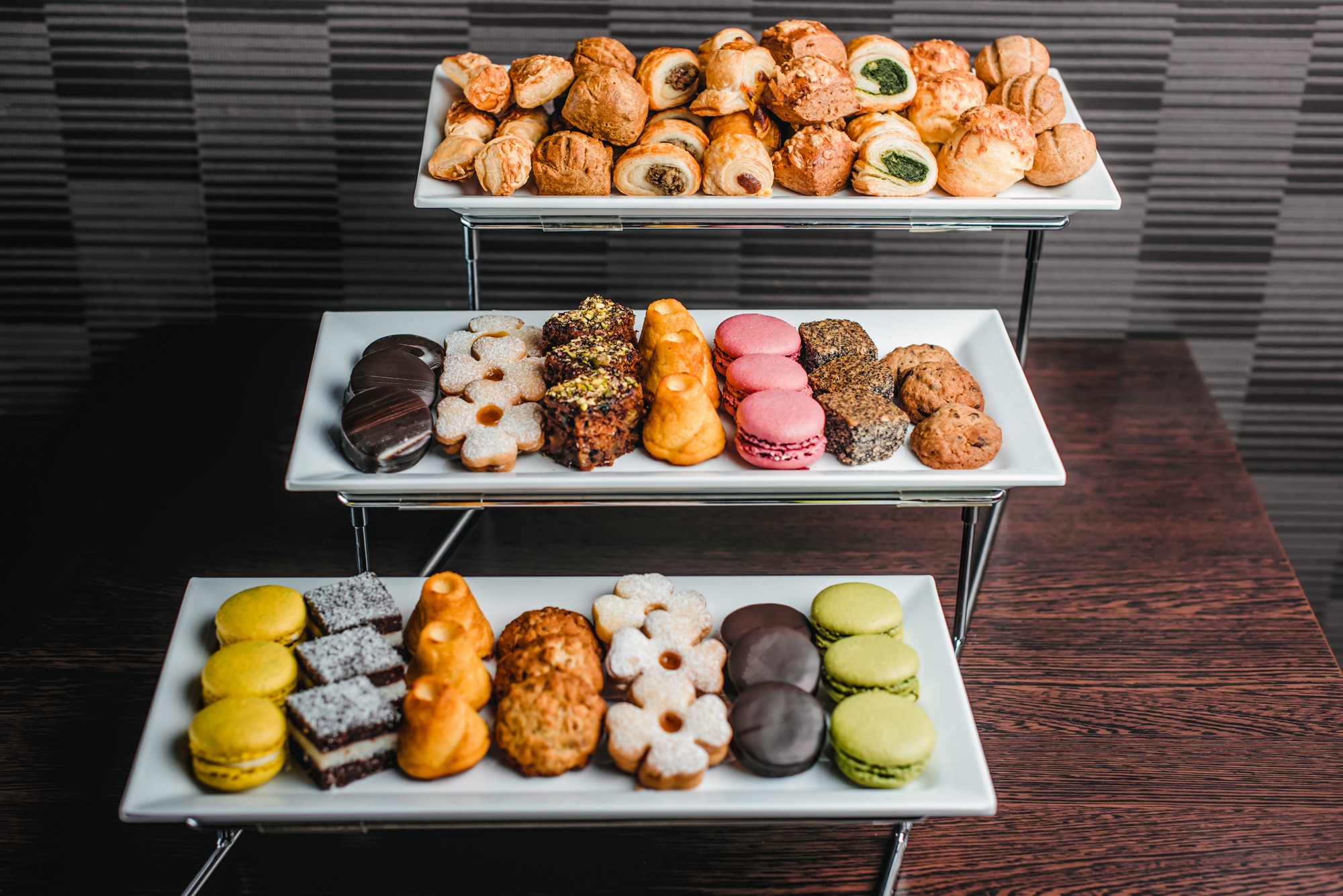Assorted pastries, macarons, cookies, and desserts displayed on tiered platters for hotel catering.