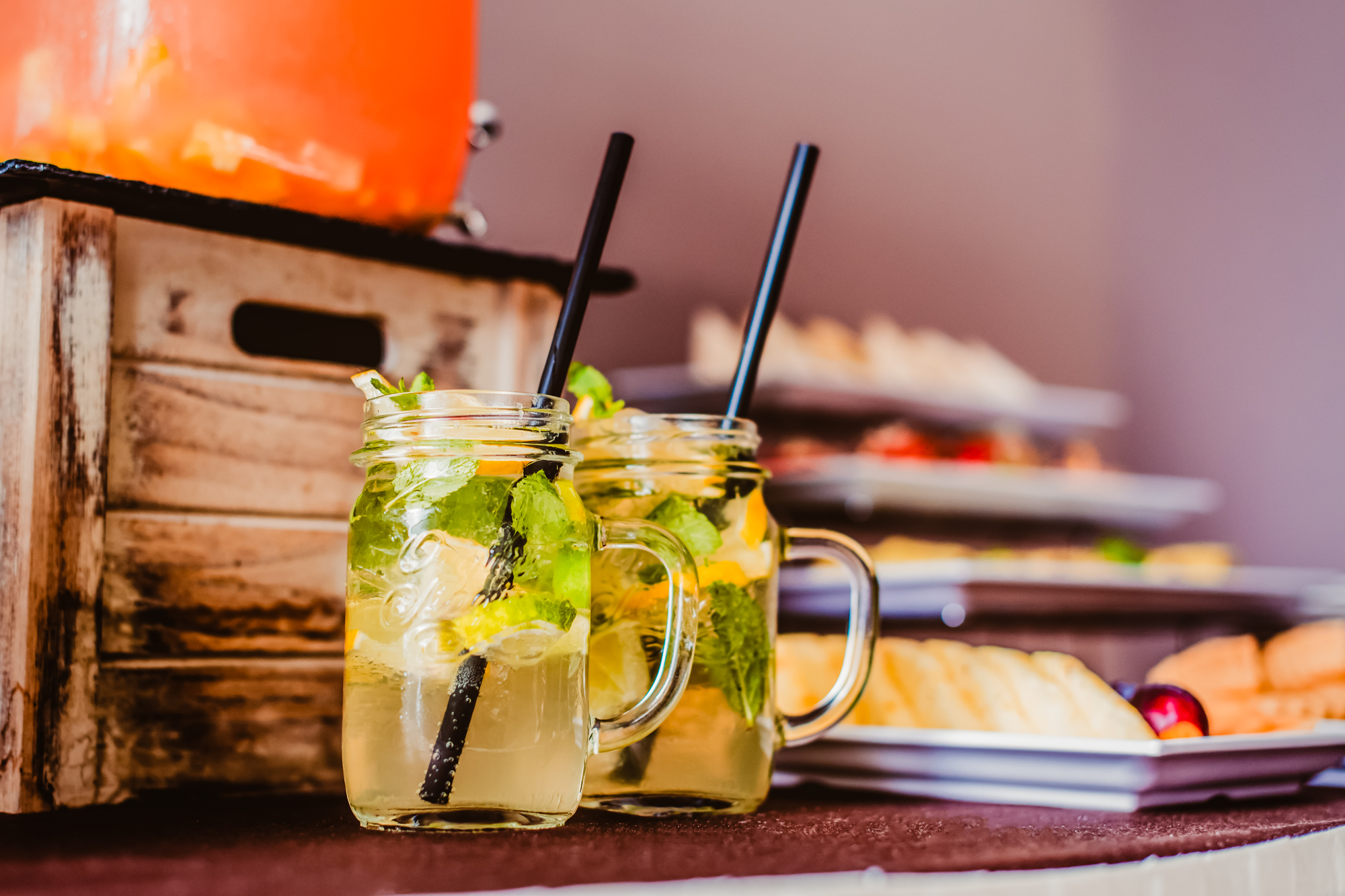 Mason jar home made lemonades with mint, lemon, and ice served beside a hotel canapé buffet display.