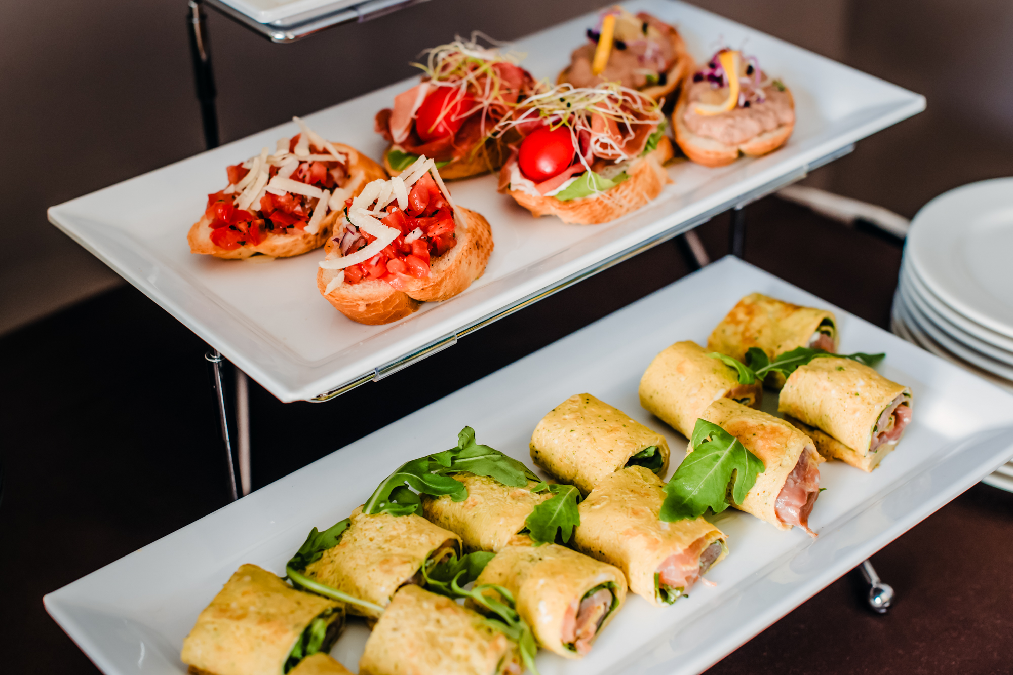 Gourmet canapé selection with bruschetta and salmon wraps served on white platters at a hotel event.