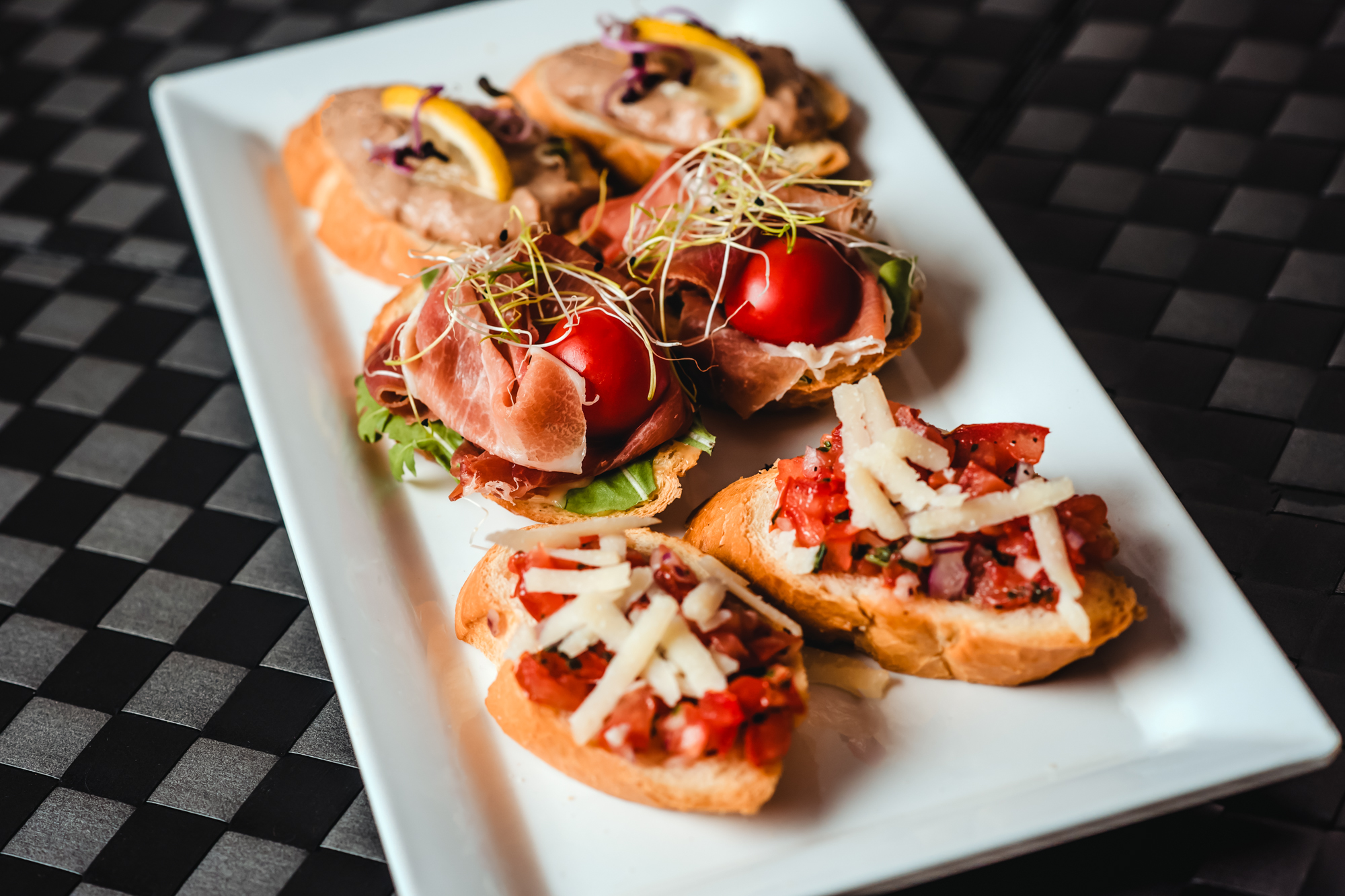 Bruschetta topped with tomatoes, prosciutto, and pâté appetisers served on a white rectangular plate at Rubin Wellness & Conference Hotel Budapest.
