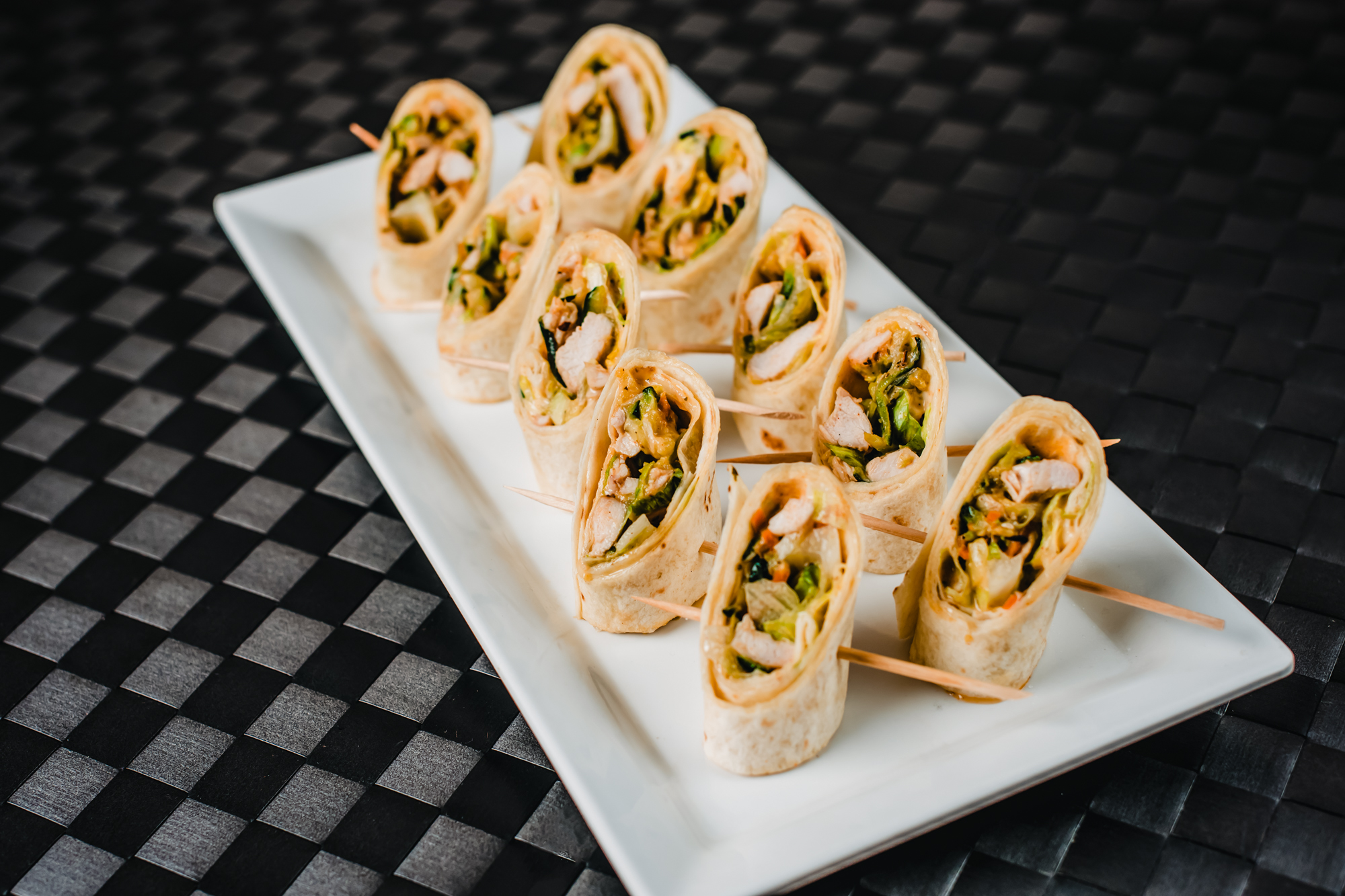 Chicken tortilla wrap bites with vegetables and sauce arranged on a white serving platter.