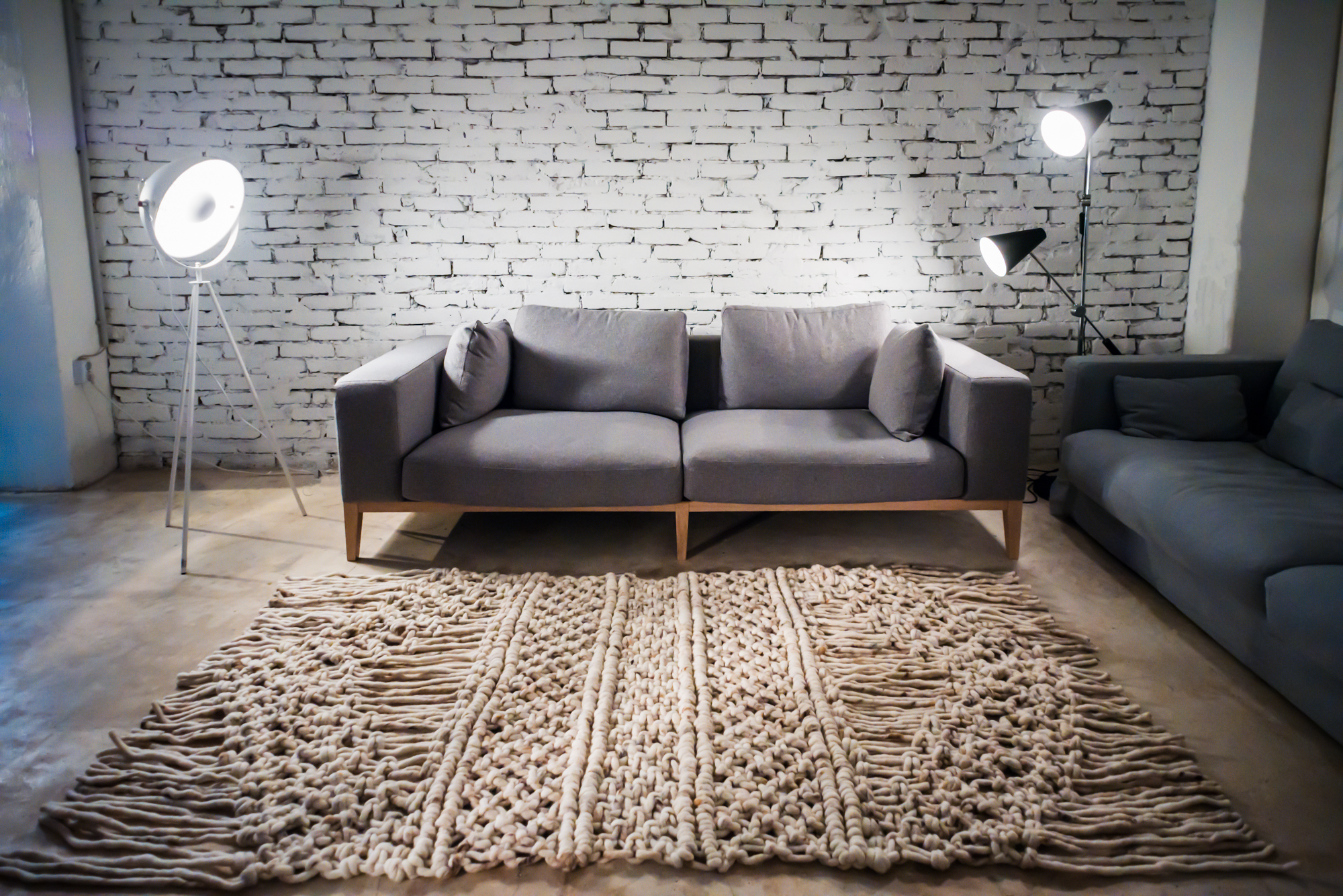 Minimalist living room with white brick wall, grey sofas, and textured wool rug.