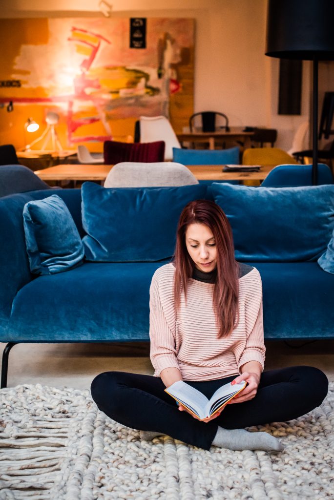 Woman reading on a textured wool rug in front of a blue velvet sofa.
