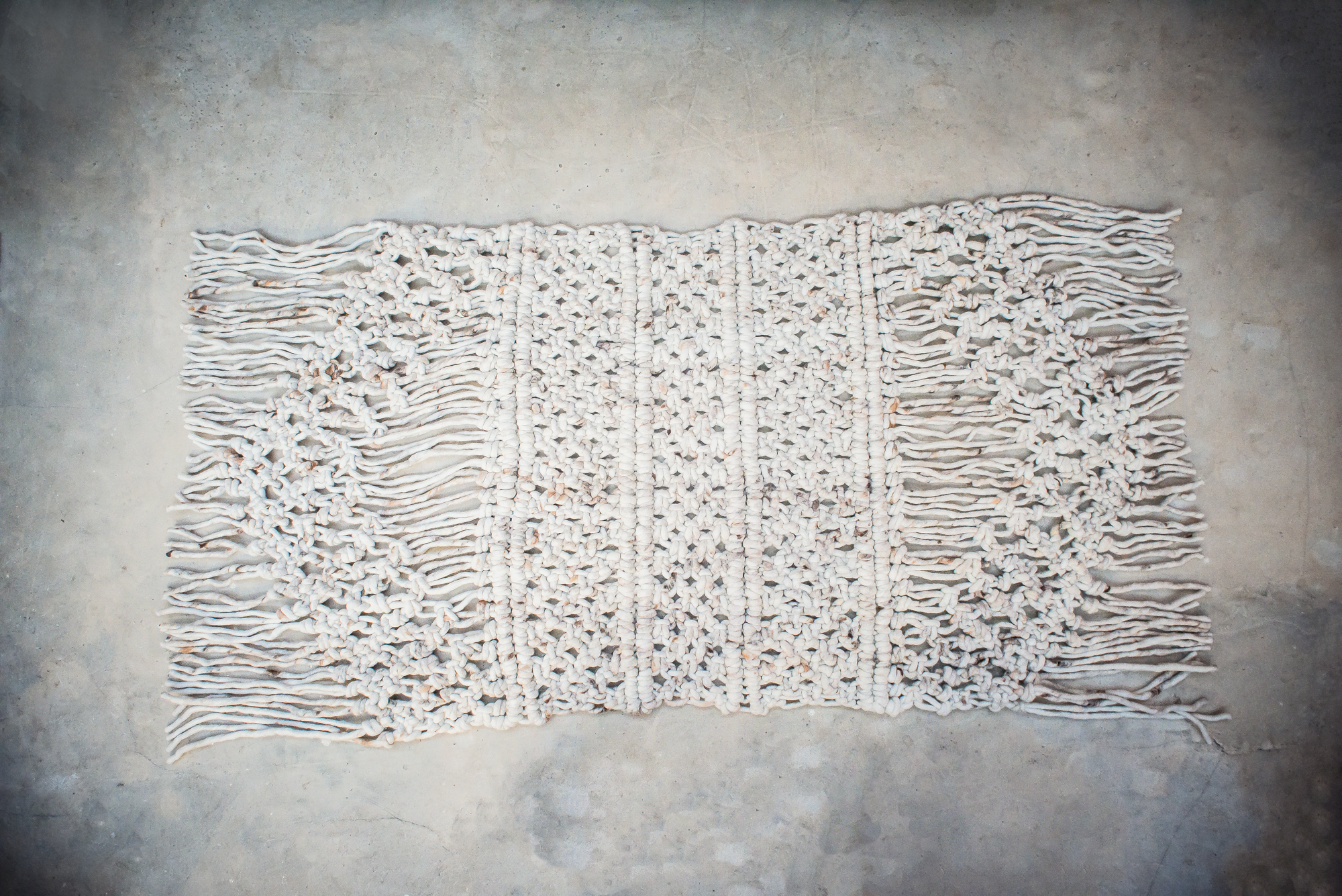 Textile product photography of overhead product photo of handmade wool rug with thick braided tassel details.