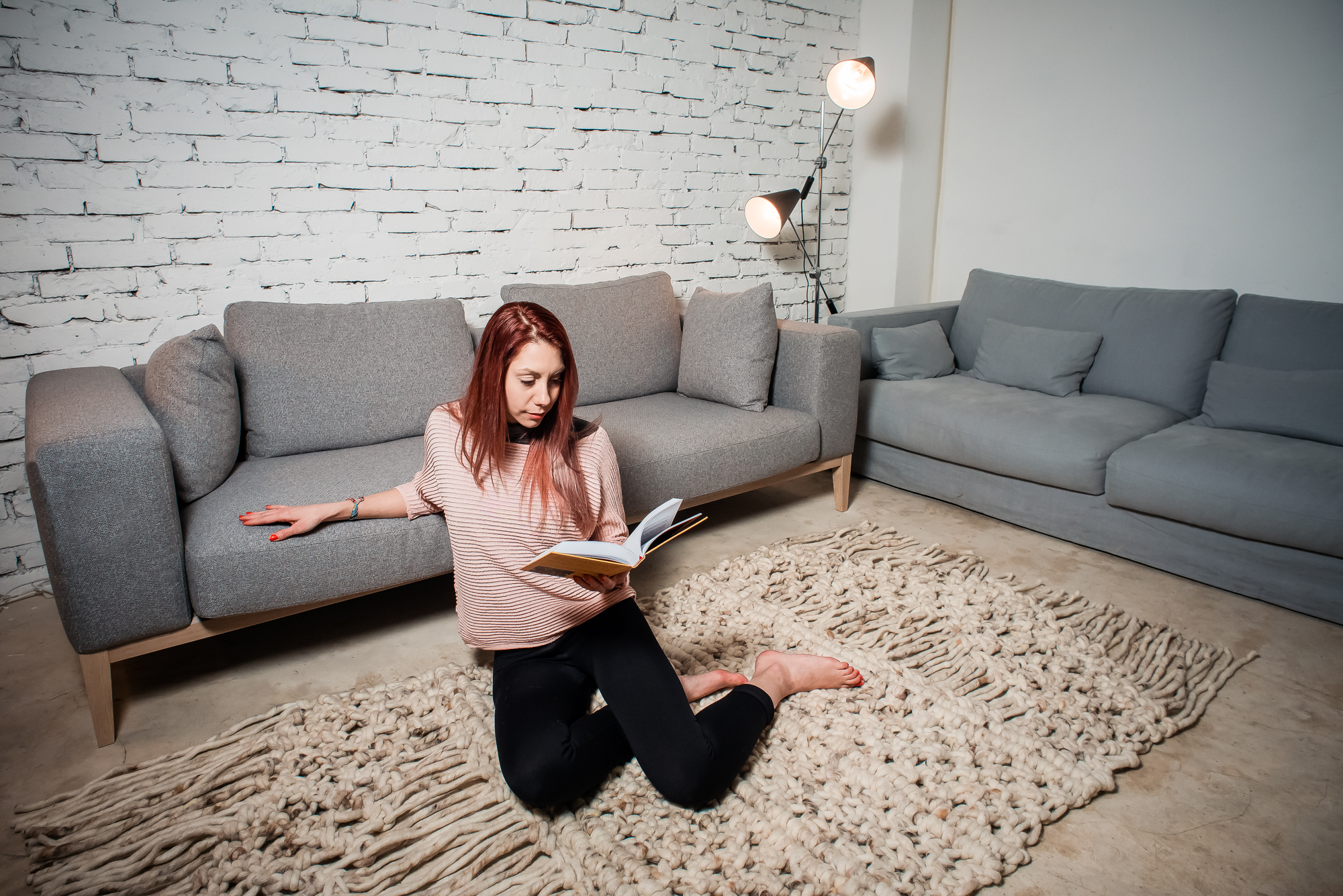 Woman reading a book on a chunky woven rug in a modern living room interior.