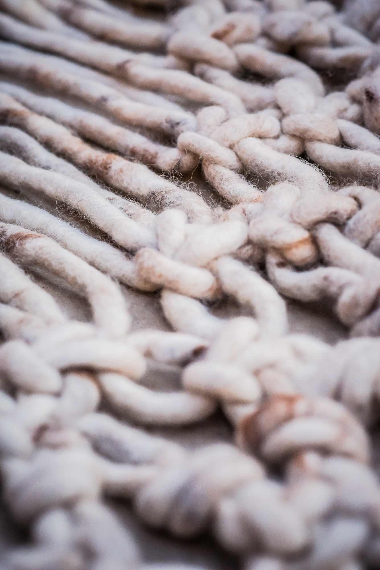 Textile product photography of macro detail of soft handwoven wool rug fibres and knotted fringe pattern.