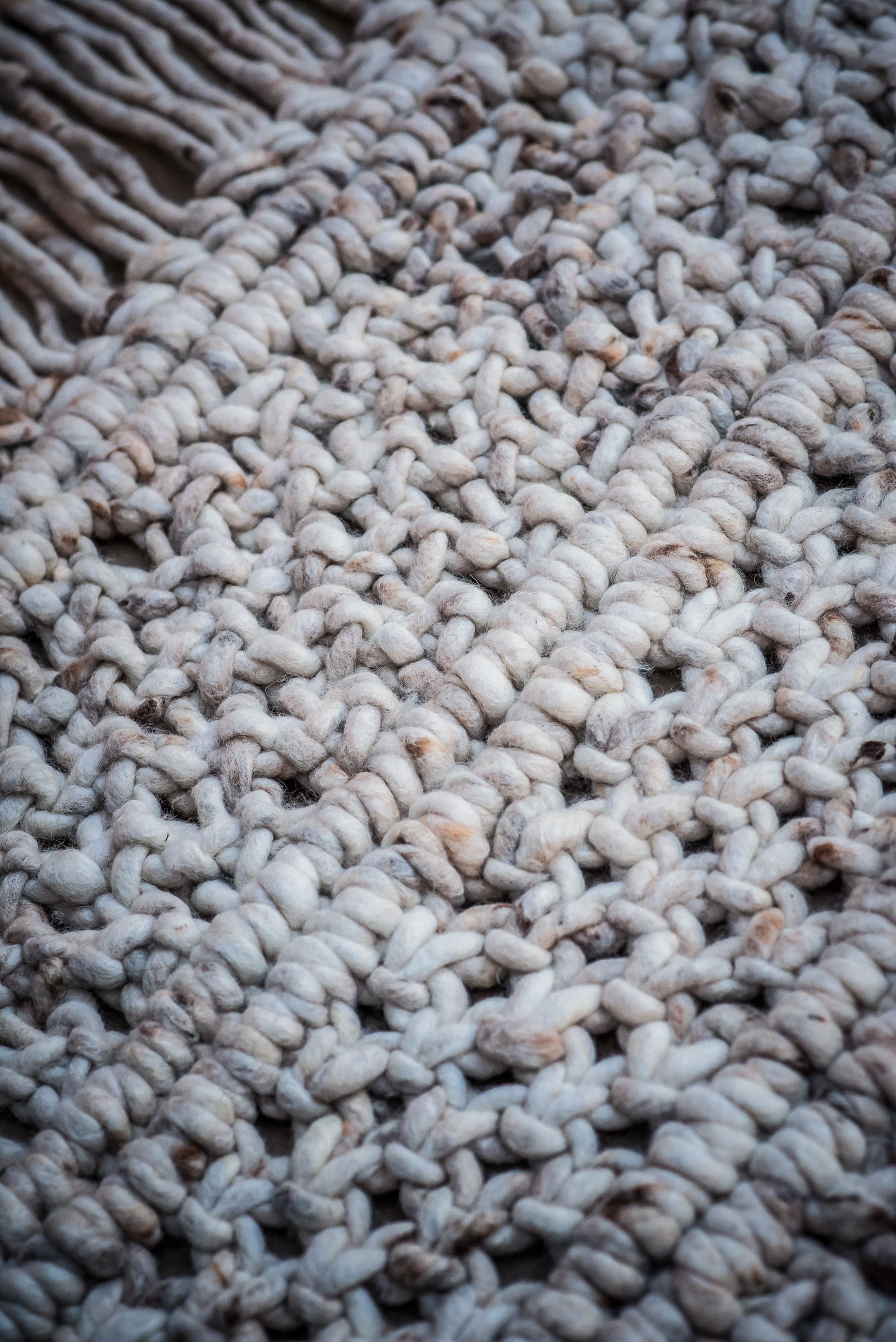 Textile product photography of a detailed texture of cream woven rug with thick braided wool strands and handmade pattern.