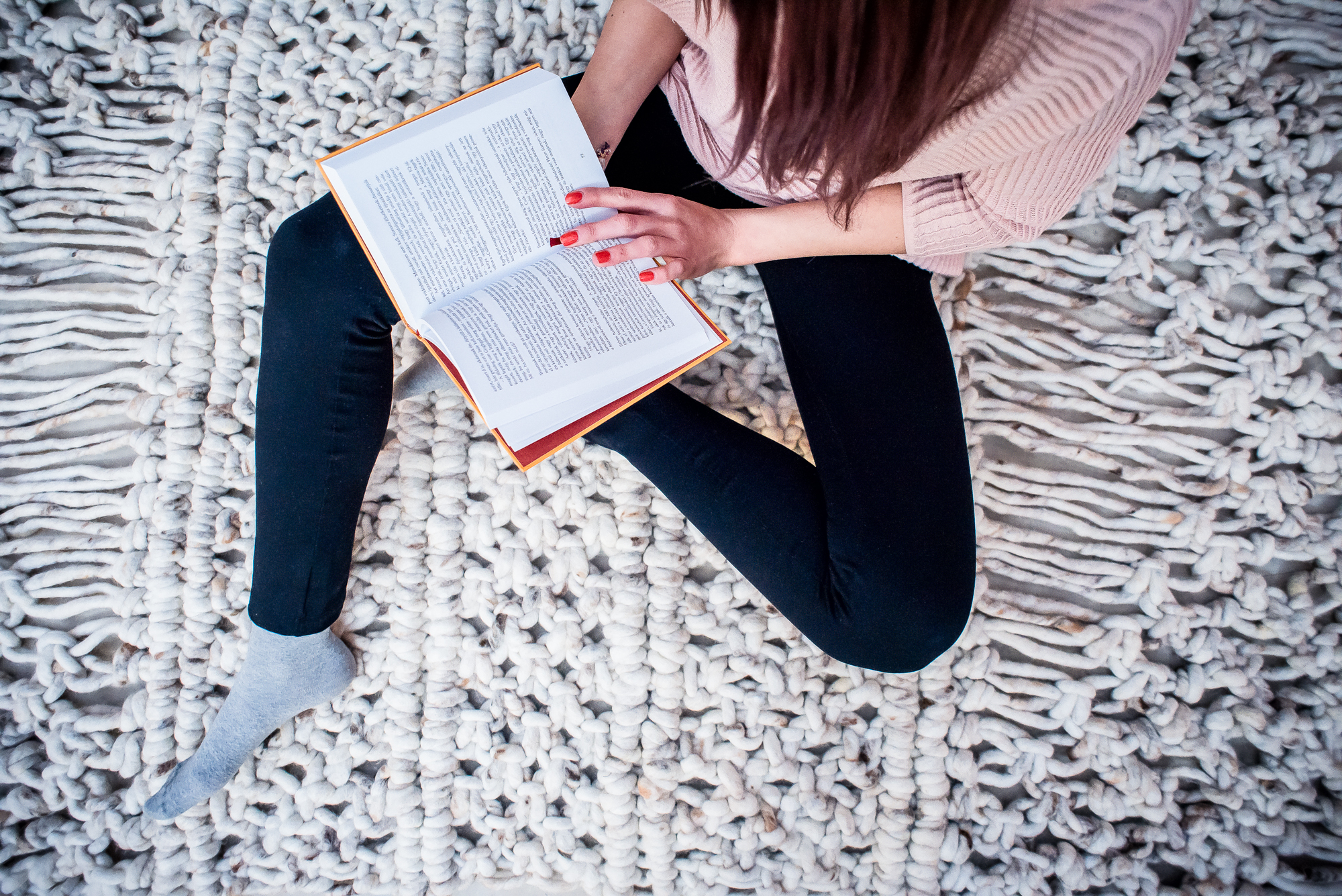Textile product photography of woman reading a book while sitting on a chunky woven rug in a cosy modern interior.