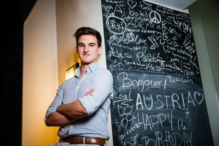 Young professional stands confidently beside a chalkboard wall covered in handwritten messages.