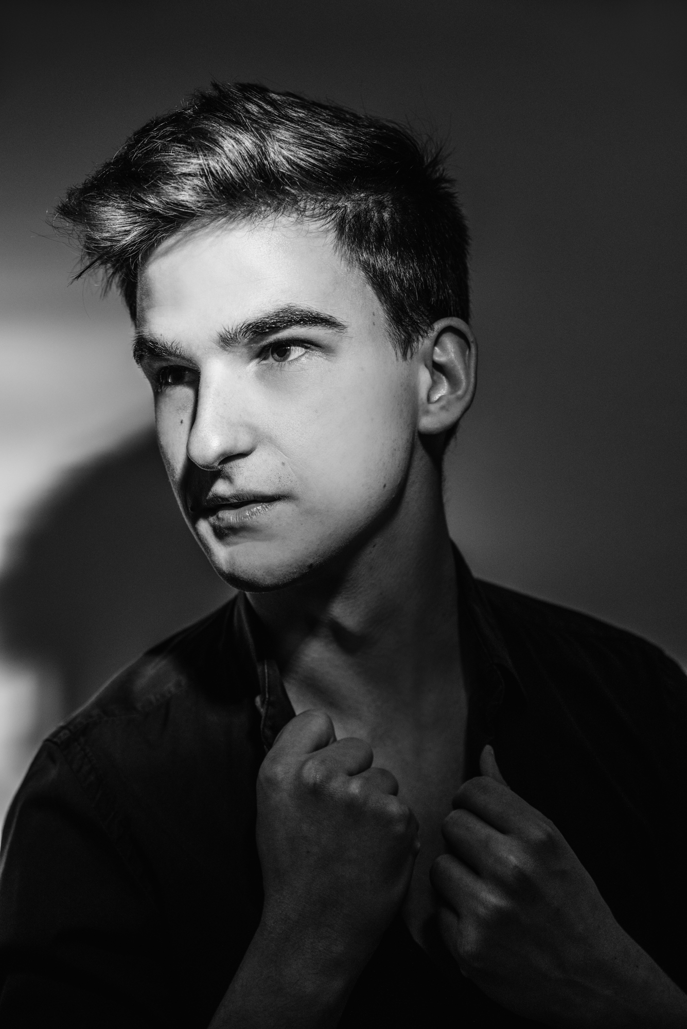 Moody black and white portrait of Ádám with dramatic side lighting and open collar.