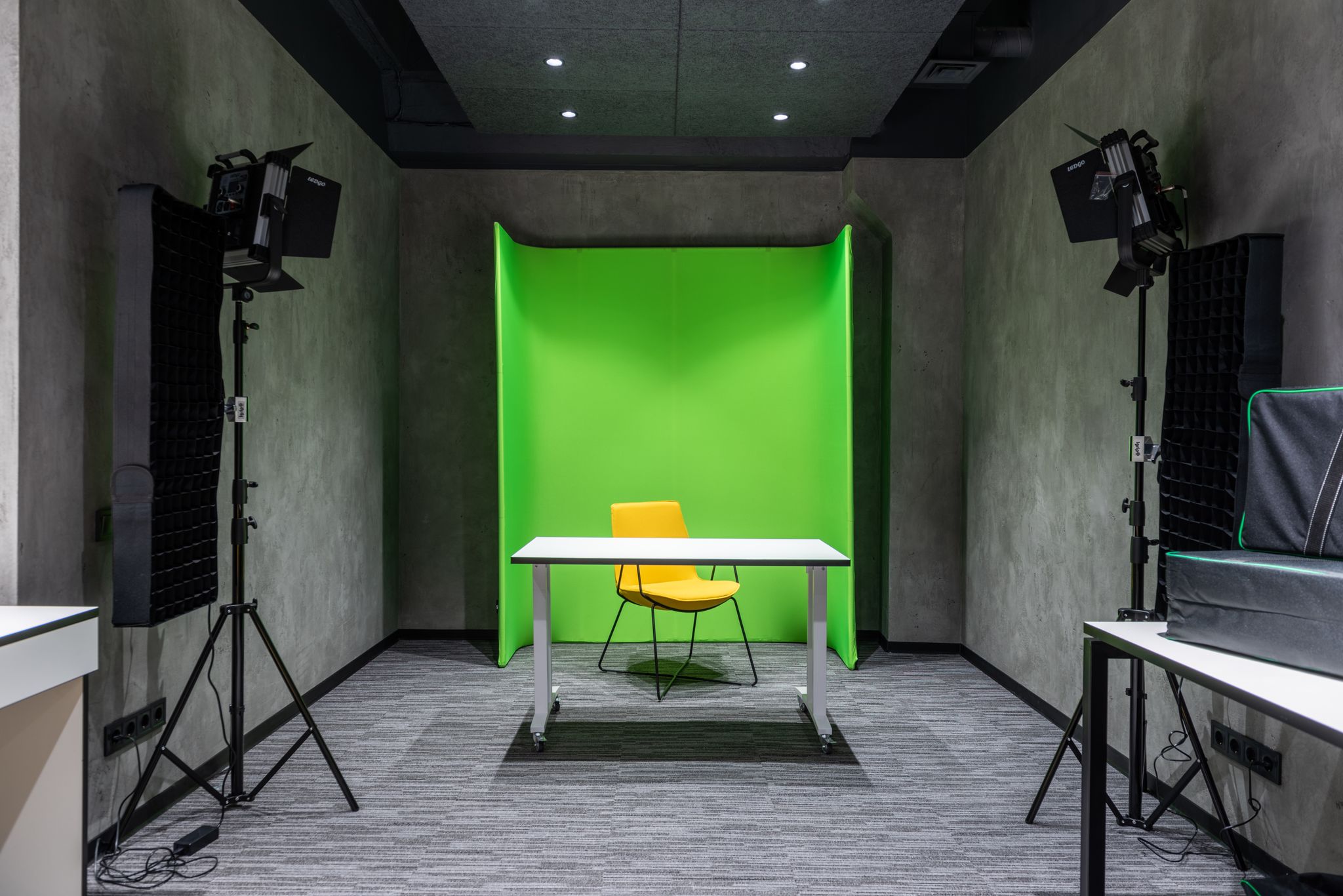 Comfortable yellow chair at white table placed near green wall in spacious modern studio with contemporary lighting equipment and professional supply