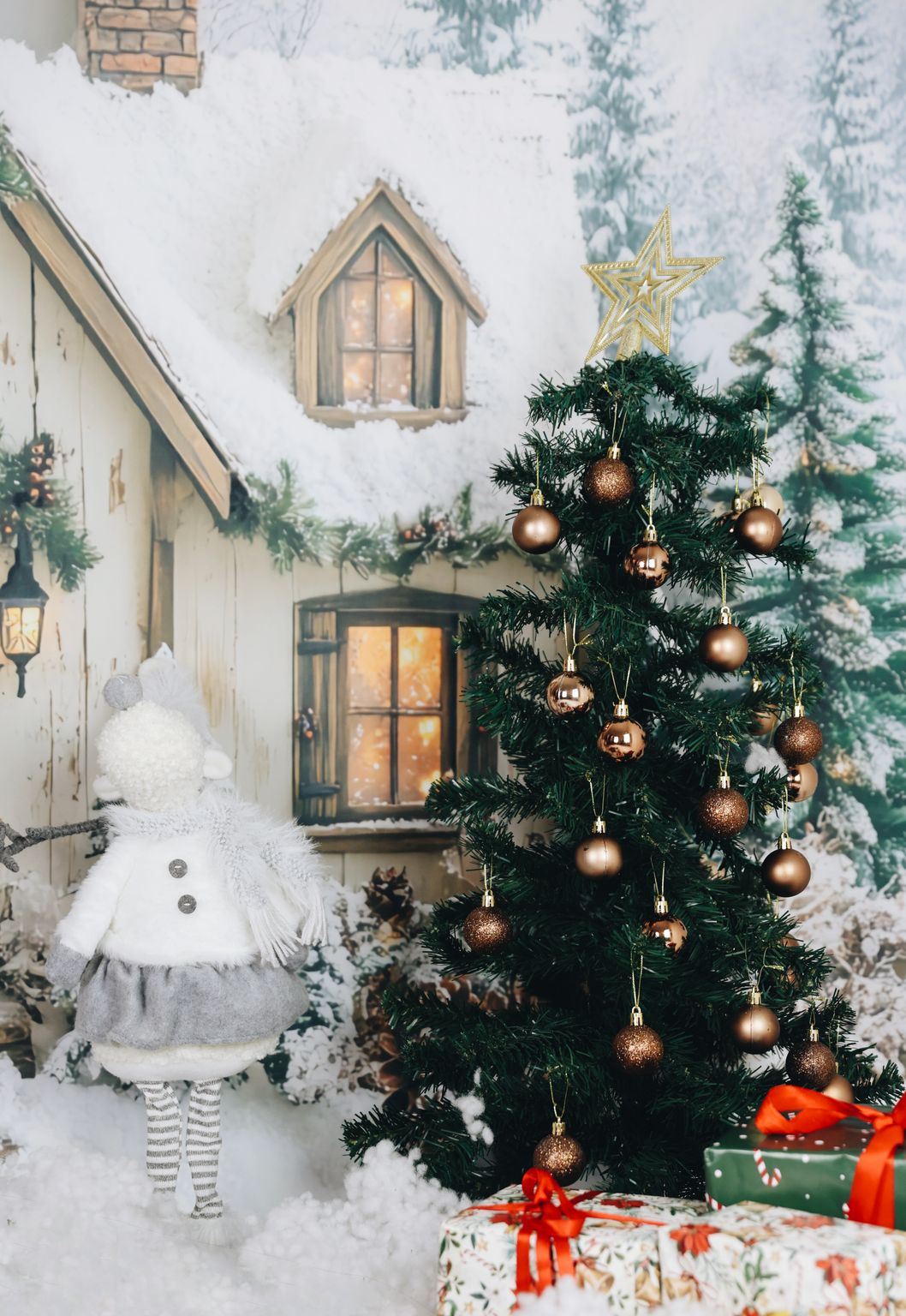 Festive winter scene with Christmas tree, doll, and gifts by a snowy house.
